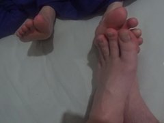 two friends playing footsies with naked feet on the bed