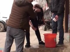 Passing stranger guys help a girl wash her long hair on the street.